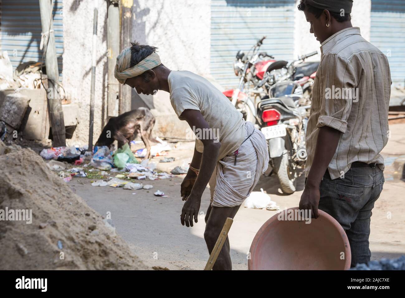 Udaipur, Inde - 05 mars 2017 : Deux jeunes hommes recueillir du sable et de l'exécuter pour fabriquer du béton. Le gars l'air fatigué. Banque D'Images