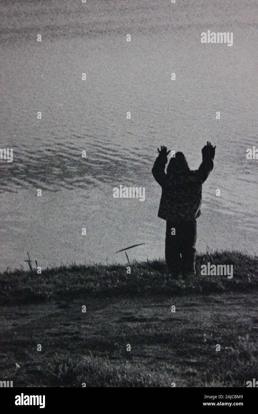 Belle photographie noir et blanc des années 1970 d'un enfant de deux ans debout au bord du lac et atteignant Banque D'Images