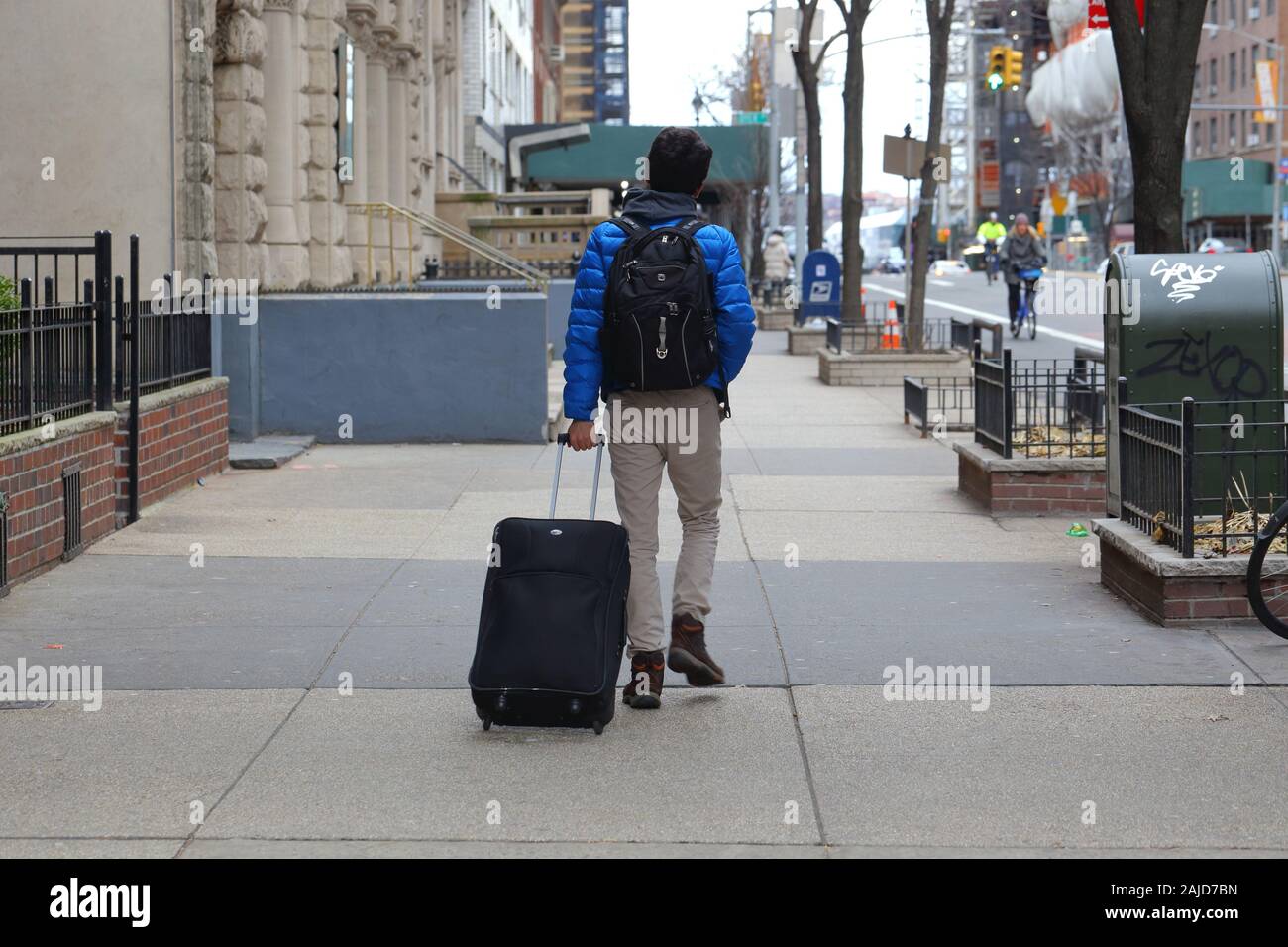 Une personne en fauteuil roulant d'une valise roulant sur un trottoir à New York, NY Banque D'Images