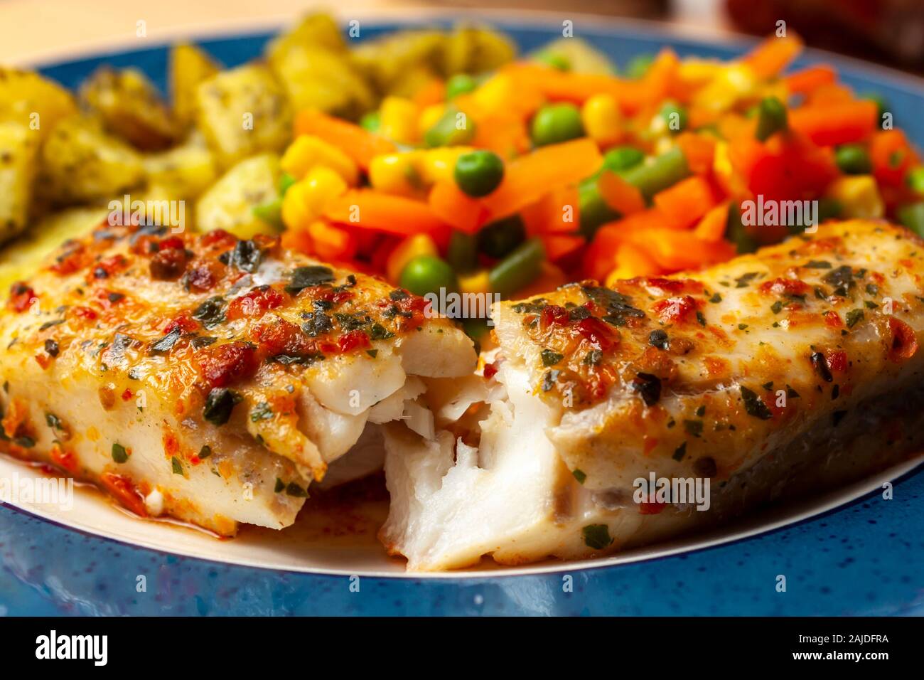 Goberge de l'chargrille poisson recouvert d'une sauce aux fines herbes et tomates sur une plaque avec un mélange de légumes et pommes de terre Banque D'Images