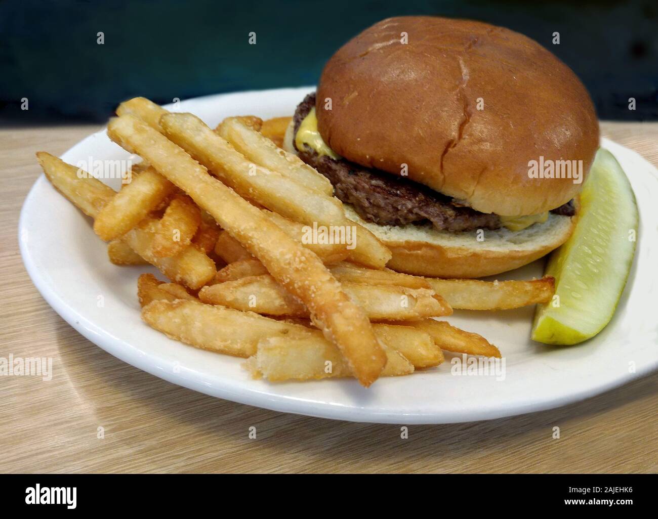 Hamburger juteux sur un petit pain avec du fromage, des frites et une tranche de cornichon Banque D'Images