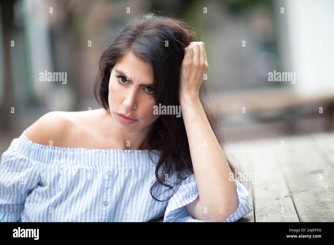 Une belle jeune femme assise à la table dans un parc de la ville, regardant au loin Banque D'Images