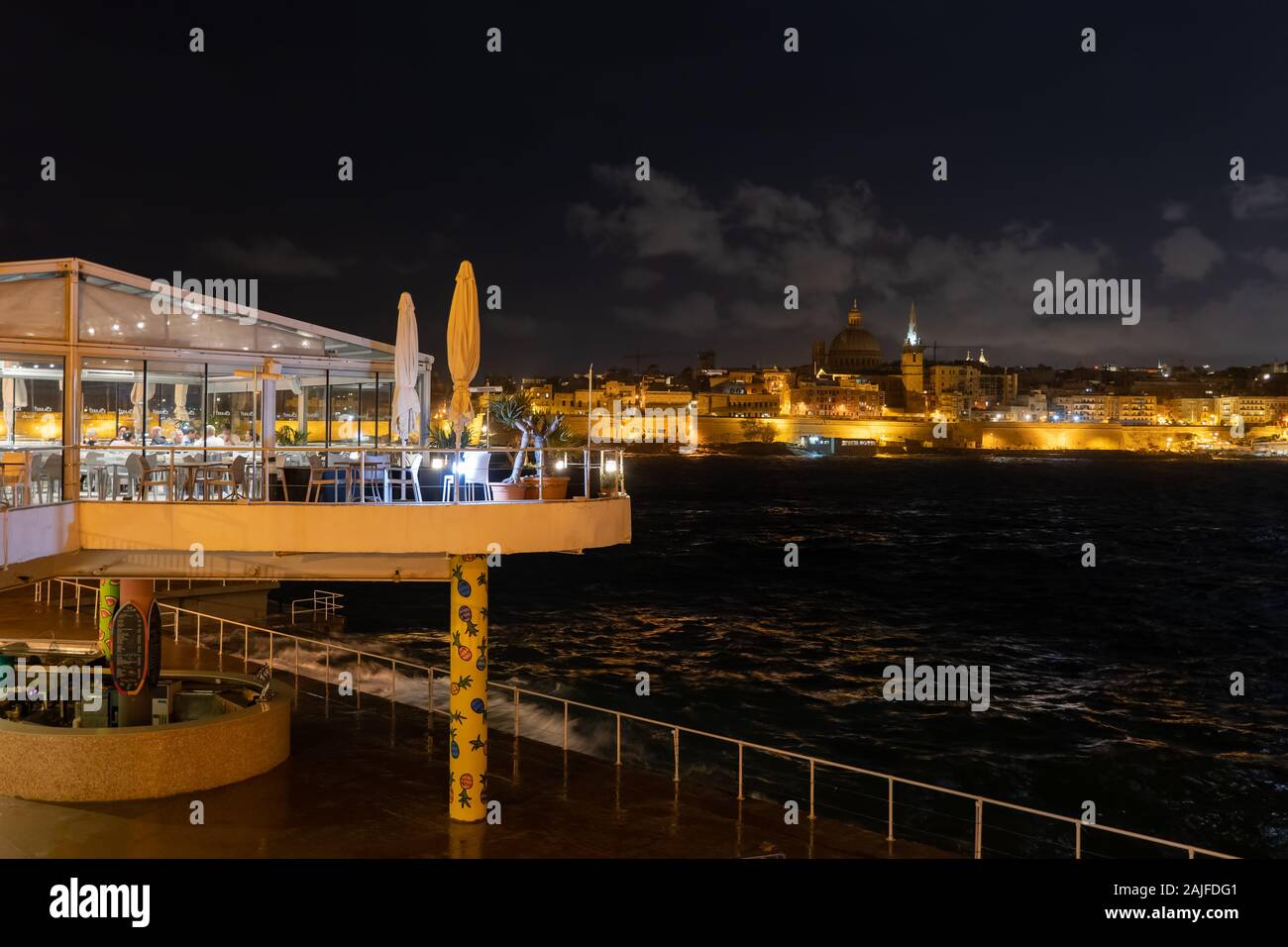 Restaurant en bord de mer dans la ville de Sliema à Malte dans la nuit, les lumières de la ville de La Valette sur l'horizon. Banque D'Images