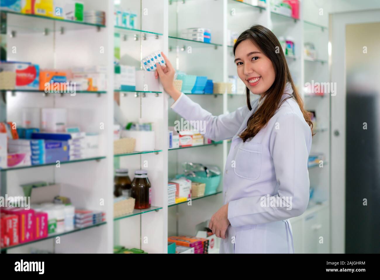 Jeune femme asiatique pharmacien avec un beau sourire amical choisir la médecine de la capsule et à la recherche à l'appareil photo dans la pharmacie en ligne. La médecine, pharmaceuti Banque D'Images