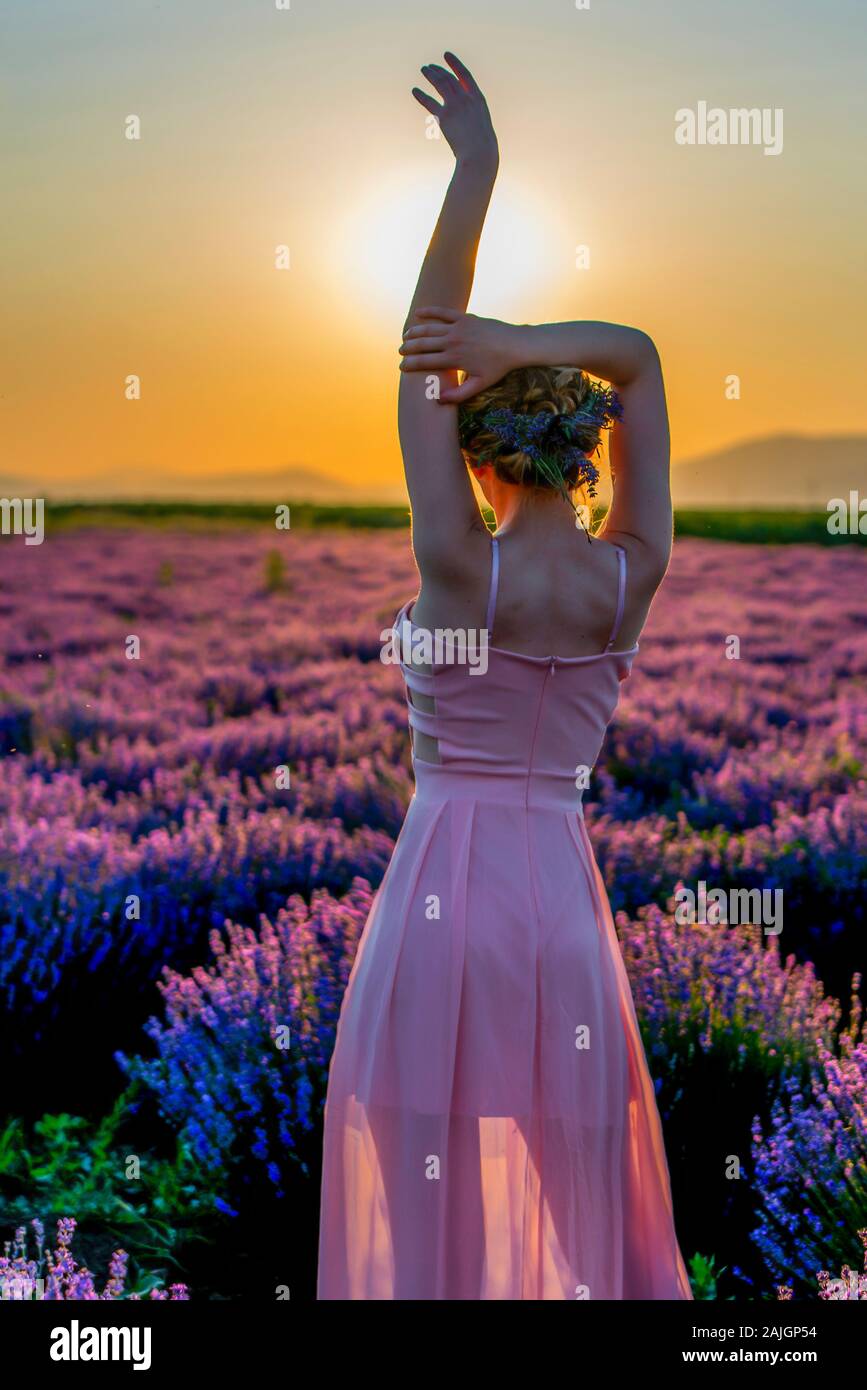 Une jeune femme se promenant dans un champ de lavande au coucher du soleil, profitant d'un beau moment dans la nature. Banque D'Images