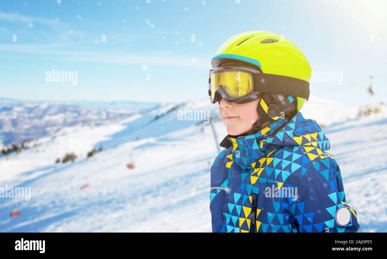 Garçon avec casque de ski, lunettes vert jaune et bleu au centre de ski. Pistes de ski et en arrière-plan. À côté de l'espace de copie Banque D'Images