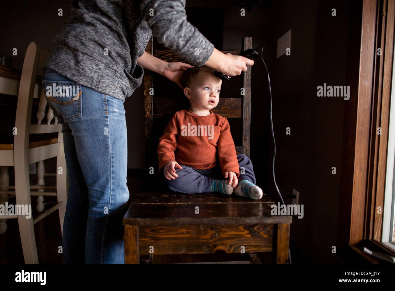 Jeune garçon se rabaisser la coupe de la cheveux de la mère sur la chaise Banque D'Images