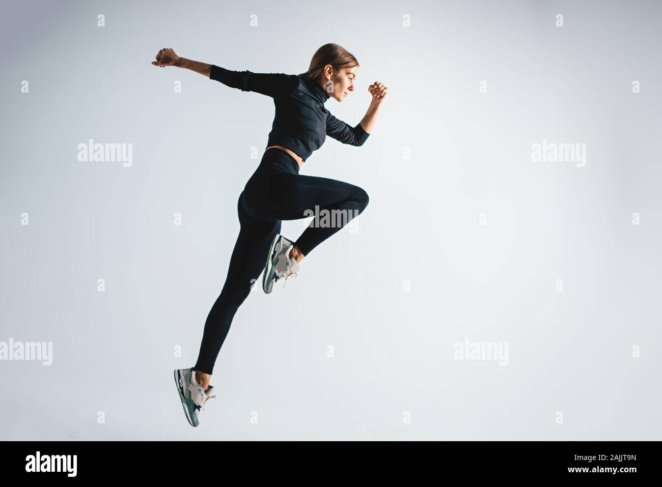 Charismatique sportive femme sautant et tournant contre l'arrière-plan de couleur blanche. Jeune fille sportive dans les sauts moment en studio Banque D'Images