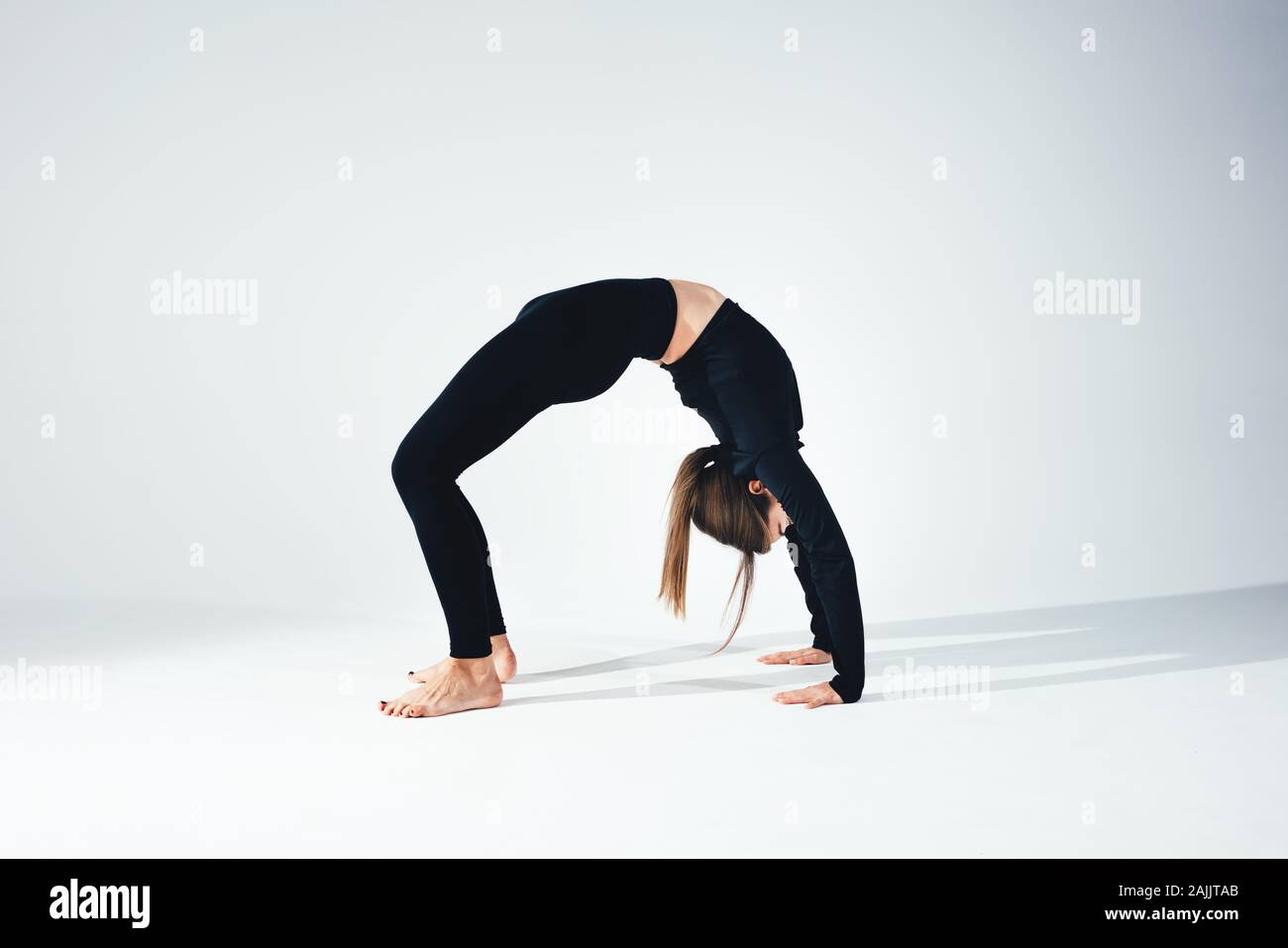 Yoga Fitness girl wearing sportswear slim noir faisant des exercices d'étirement en salle blanche. Vue de côté de la femme faisant s'étend contre vide background Banque D'Images