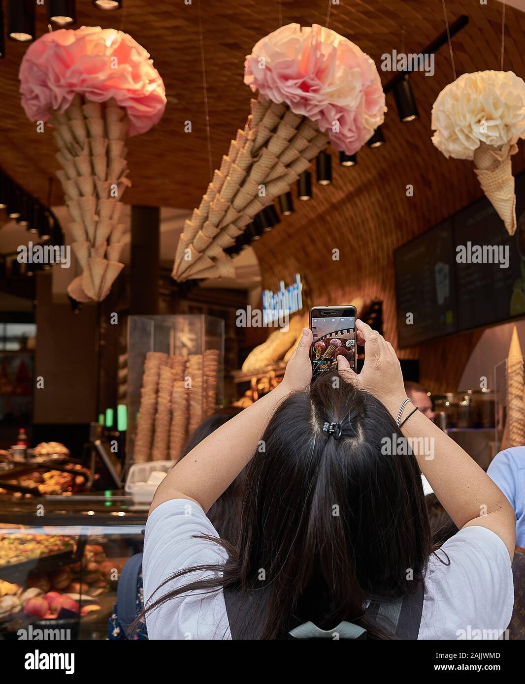 La femme prend un coup de téléphone portable de cônes de glace de grande taille faits de dizaines de gaufres et de papier rose dans ce salon du centre-ville de Munich, en Allemagne Banque D'Images