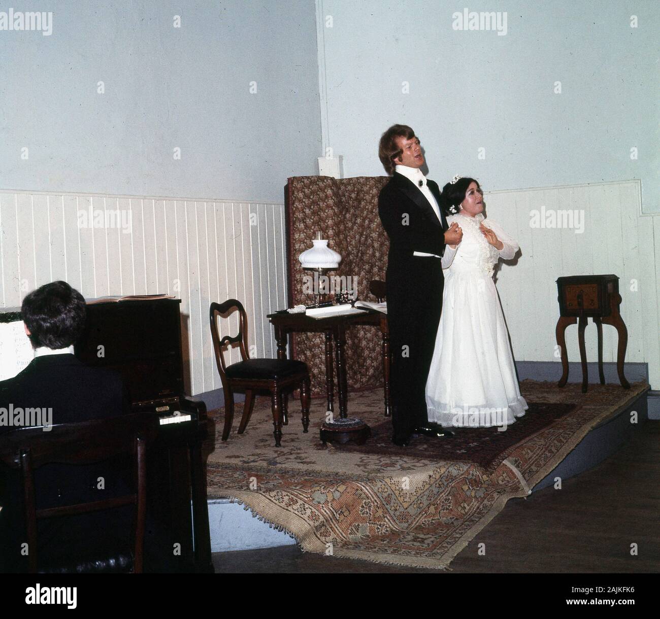 Années 60, historique, un trio de Wexford, Irlande, avec un homme et une femme en costume de cravate noire sur une petite scène ressemblant à une salle de front victorienne, chantant ensemble, accompagné d'un homme jouant un piano. Banque D'Images