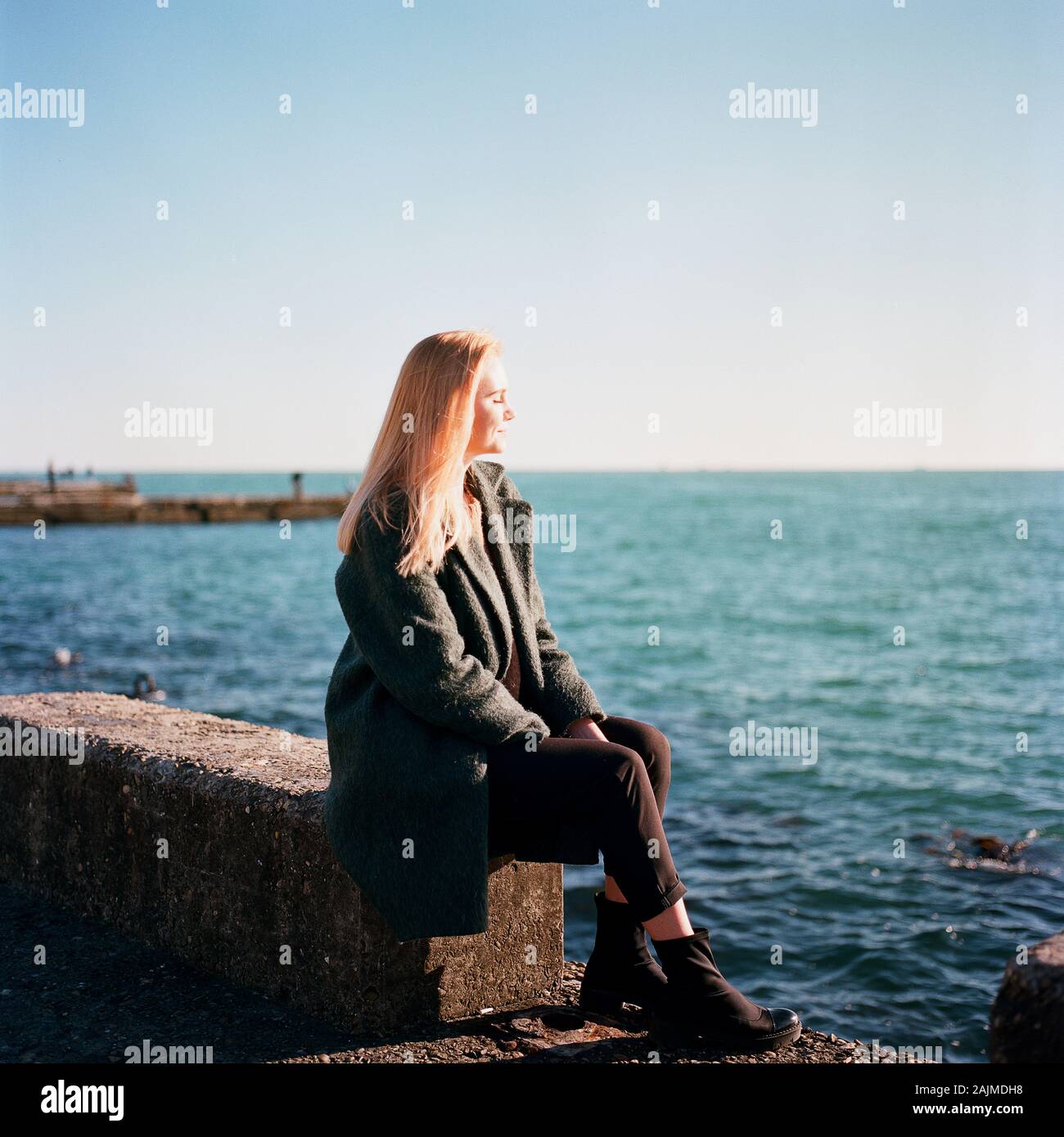 Une belle femme assise seule sur la jetée et sourit Banque D'Images