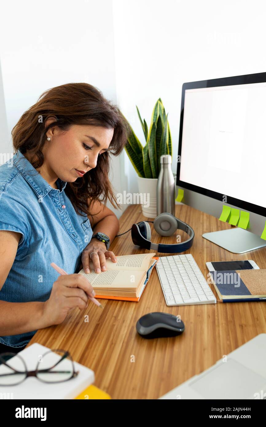 Femme de 40 ans, bien réfléchie, lisant assis devant l'ordinateur Banque D'Images