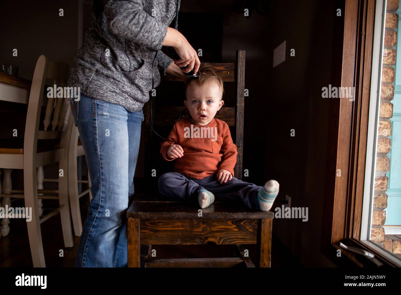 Un tout-petit garçon se coupe la coupe de cheveux à la maison par sa mère Banque D'Images