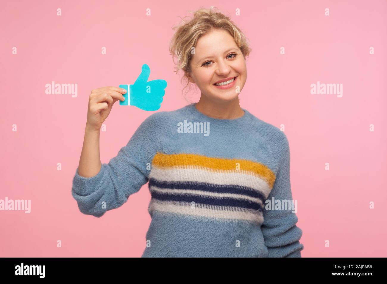 Comme bouton. Portrait of happy woman in sweater holding Thumbs up icône bleu, symbole de notification de galet, de recommandation et de bons commentaires en service social Banque D'Images