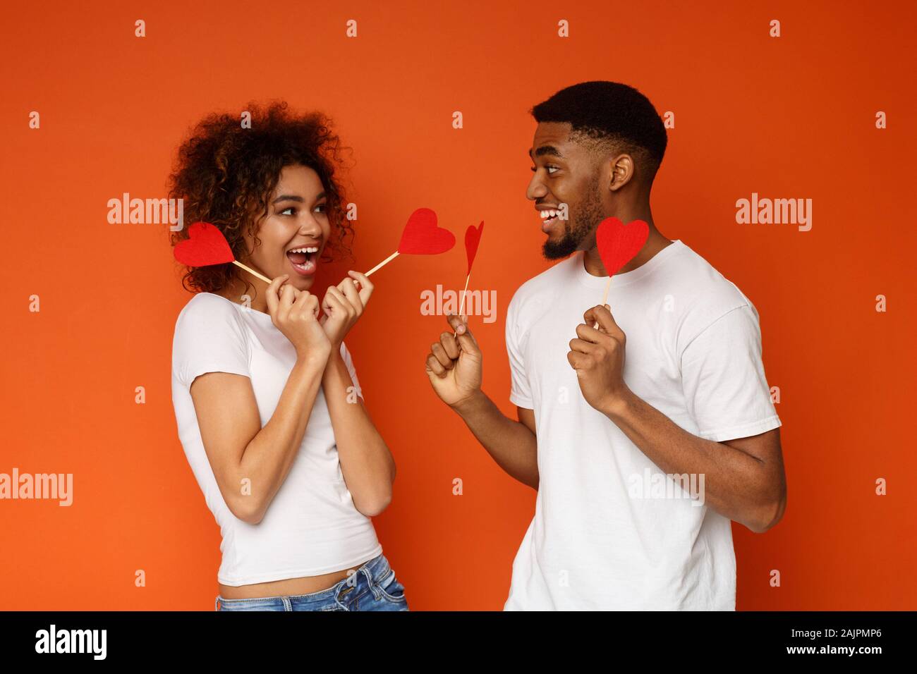 L'amour est autour de nous. Les jeunes aimer african american couple holding papier rouge coeurs et souriant à l'autre, fond orange Banque D'Images