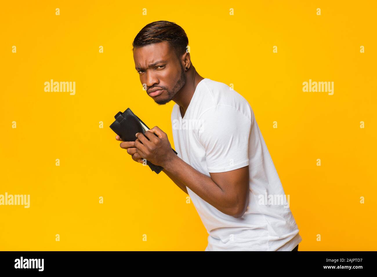 Le vol et la tire. Fraude sournoise Afro Man Holding Wallet avec de l'argent au-dessus de l'arrière-plan jaune Studio. Banque D'Images