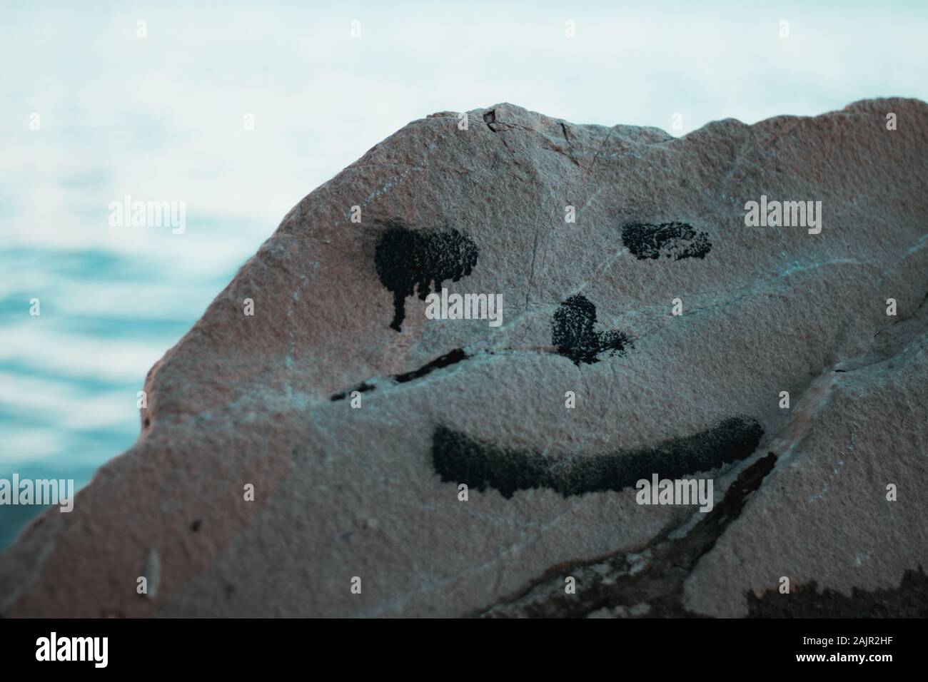 Noir étrange smiley étrange sur un rocher près de la mer, concept de faux sourire, la tristesse, l'inquiétude. Photo d'hiver froid Banque D'Images