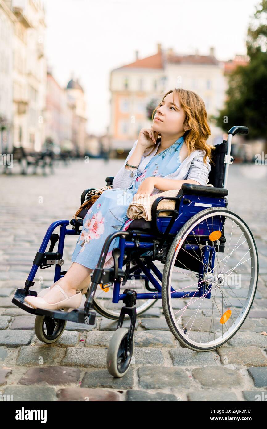 Mobilité attrayante jeune femme en robe bleue assise dans un fauteuil  roulant, à l'extérieur de la ville Photo Stock - Alamy