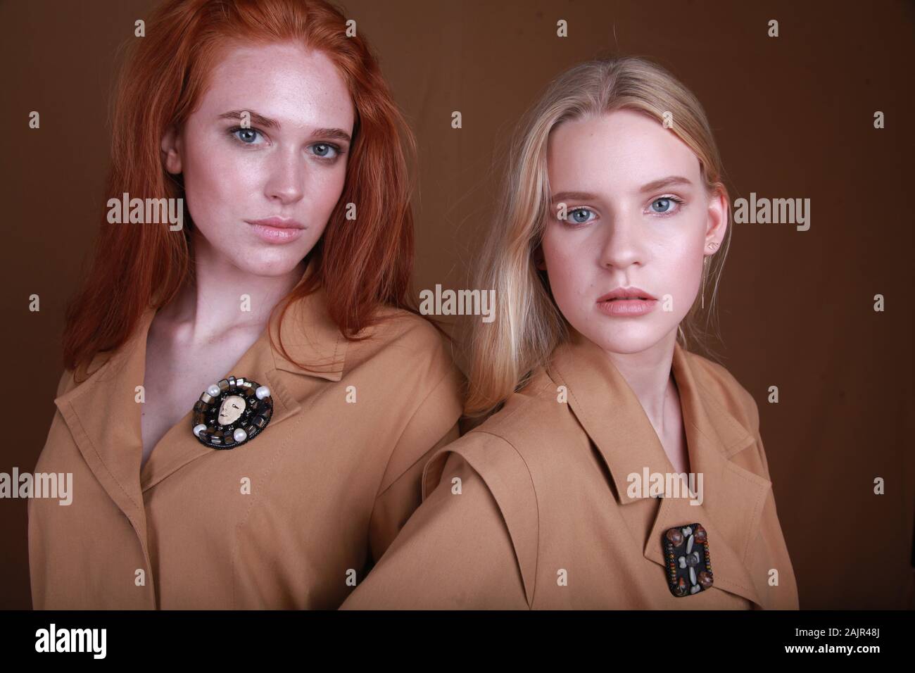 Fermer portrait de deux belles jeunes filles avec les produits de maquillage, vêtu de vêtements beige sur un fond brun. Accessoire de mode et concept. Les jeunes Banque D'Images
