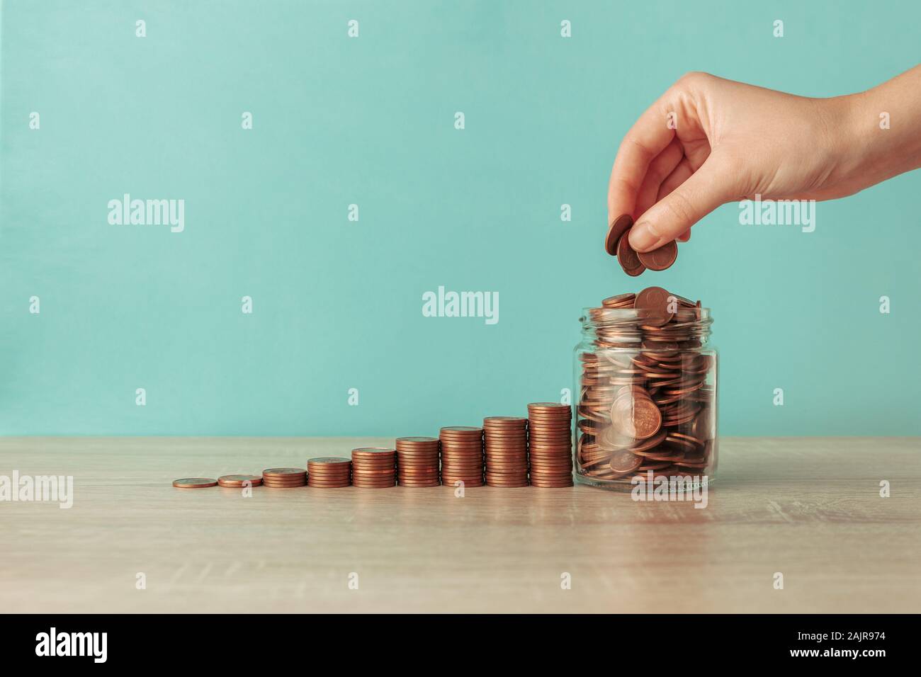 Stock photo d'un escalier ascendant de pièces sur un fond bleu avec un pot plein de pièces. A woman's hand est mettre des pièces à l'intérieur Banque D'Images