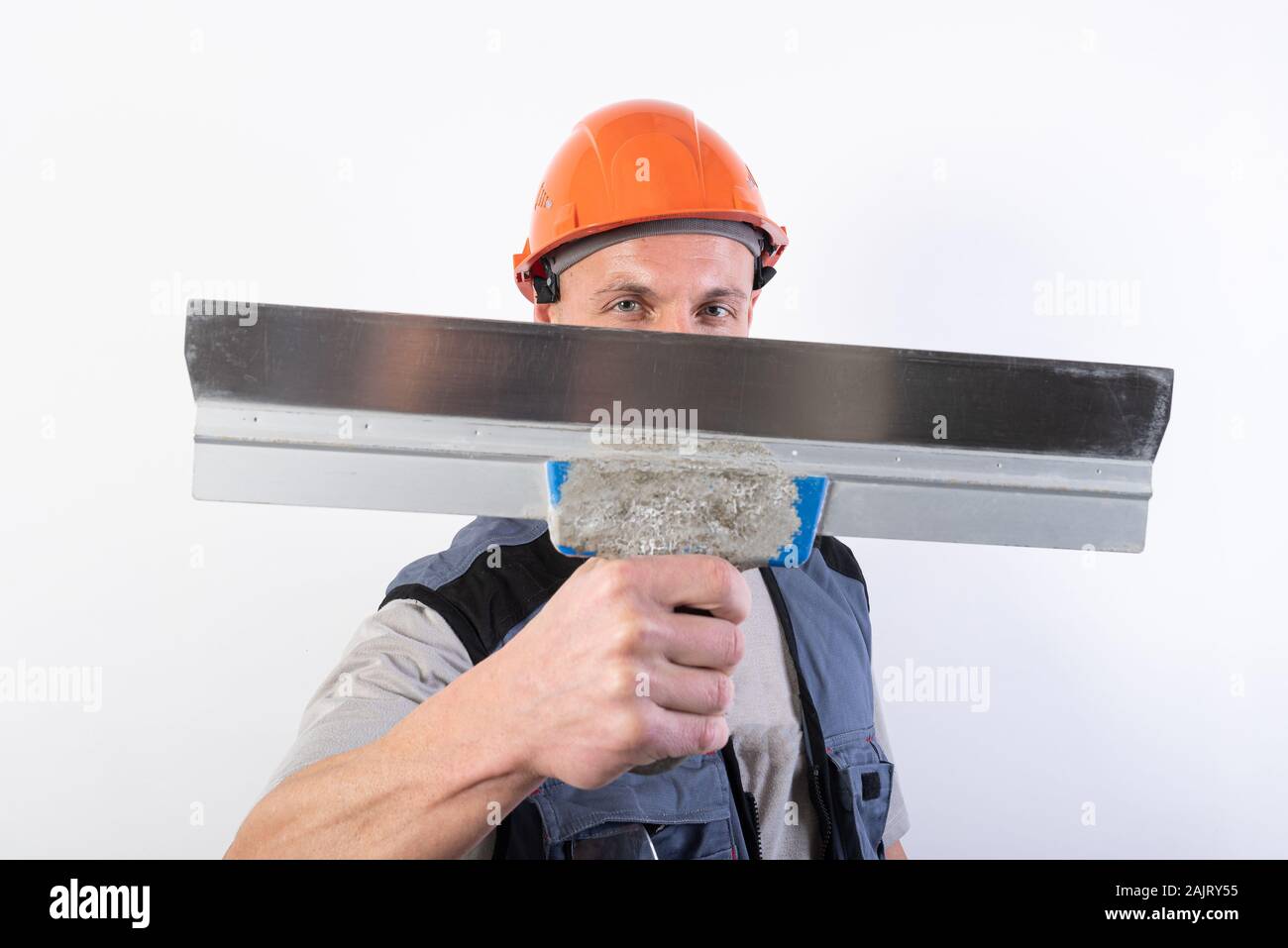 Le constructeur cache son visage derrière une spatule. Dans les vêtements de travail et casque de sécurité. Sur un fond gris clair. Banque D'Images