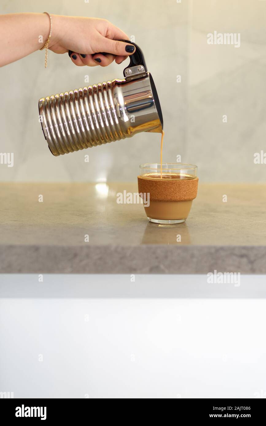 La femme est de verser le café chaud dans la cafetière en verre réutilisables Coffee cup sur le table de marbre dans la matinée. Banque D'Images