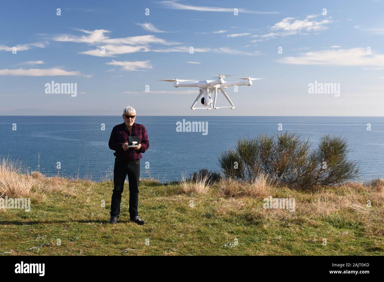 Debout sur une falaise au-dessus de la mer l'homme de plus de 50 ans avec télécommande dans ses mains exécute un drone dans le ciel blanc Banque D'Images