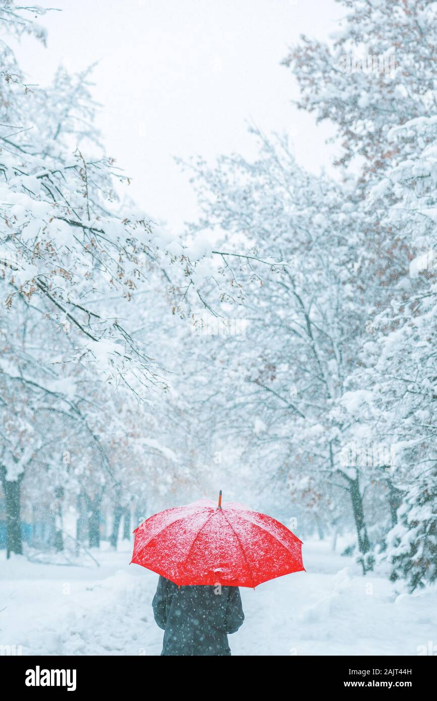 Femme sous parapluie rouge dans la neige profiter de la première neige de la saison d'hiver Banque D'Images