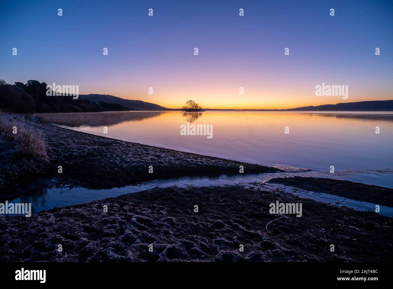 Lever du soleil d'hiver sur le calme de l'île du loch avec, d'un ruisseau et frosty shore. Burleigh Sands, le Loch Leven National Nature Reserve, Ecosse, Royaume-Uni. Banque D'Images Lever du soleil d'hiver sur le calme de l'île du loch avec, d'un ruisseau et frosty shore. Burleigh Sands, le Loch Leven National Nature Reserve, Ecosse, Royaume-Uni. Banque D'Images