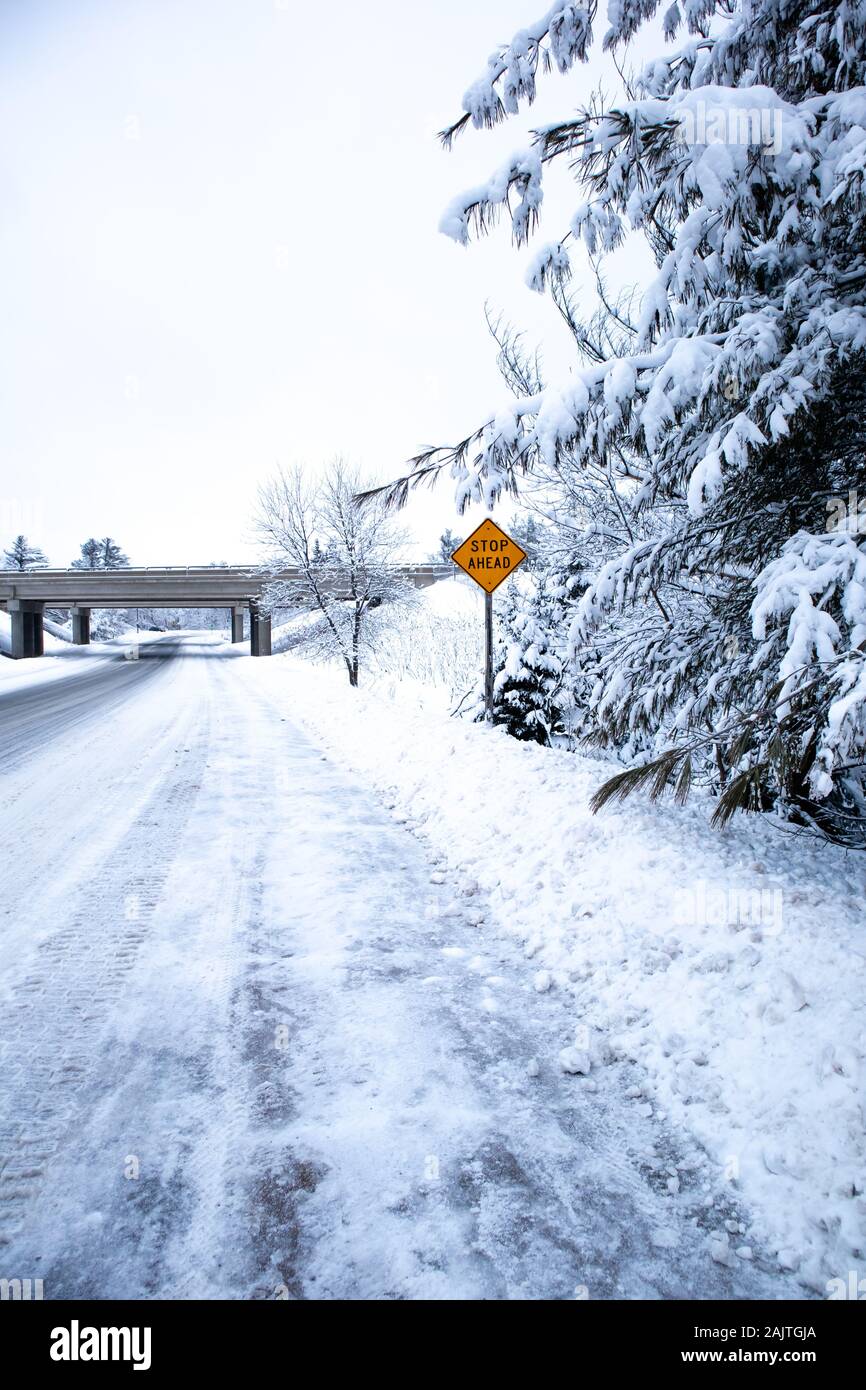 Route couverte de neige glissante et forêt dans le centre du Wisconsin en décembre avec arrêt à venir signer, vertical Banque D'Images