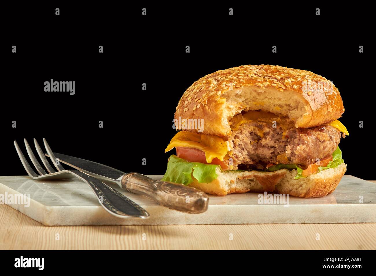 Burger d'artisanat avec fourchette et couteau sur fond noir. Cheeseburger sur plaque. Banque D'Images