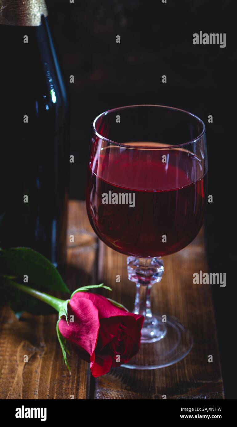 Dark définition d'un verre de vin et une rose rouge avec une bouteille en arrière-plan sur une table en bois Banque D'Images
