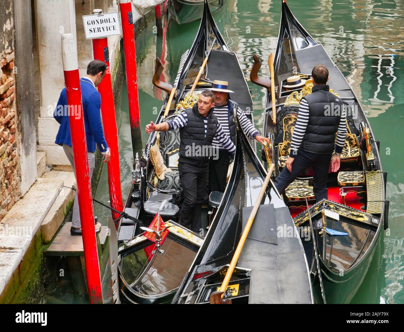 Un gondolier se prépare à aider un client à bord lorsqu'il s'approche de gondoles amarrés sur un petit canal à Venise, Italie. Banque D'Images