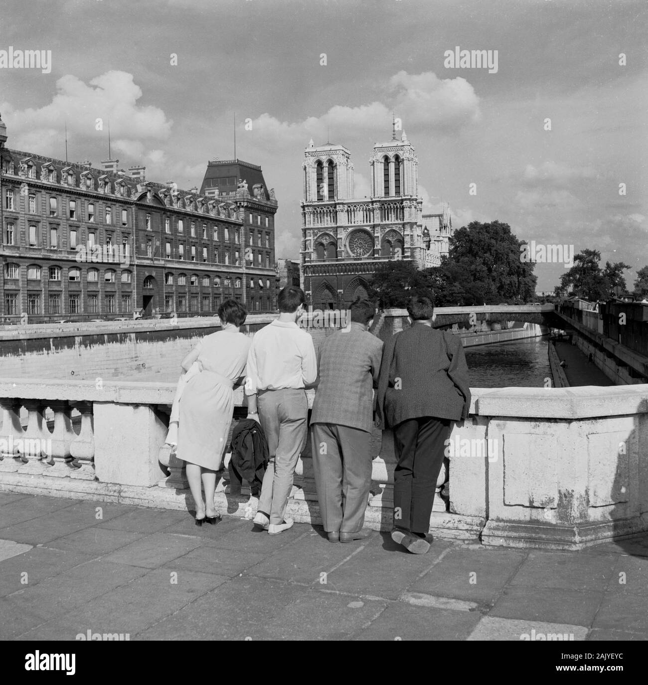 Années 1950, historique, des gens se tenant sur un pont au-dessus de la Seine en regardant le célèbre Catherdal notre-Dame au loin, Paris, France. La cathédrale gothique médiévale est l'un des monuments les plus célèbres de la ville. Banque D'Images