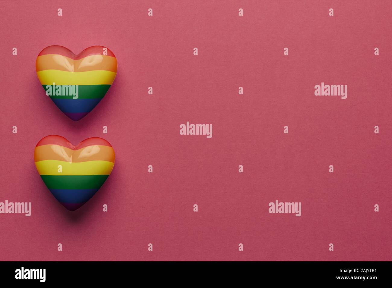 Stock photo de deux coeurs en plastique LGBT sur fond rouge. Le cœur sur le côté gauche avec un espace réservé au texte Banque D'Images