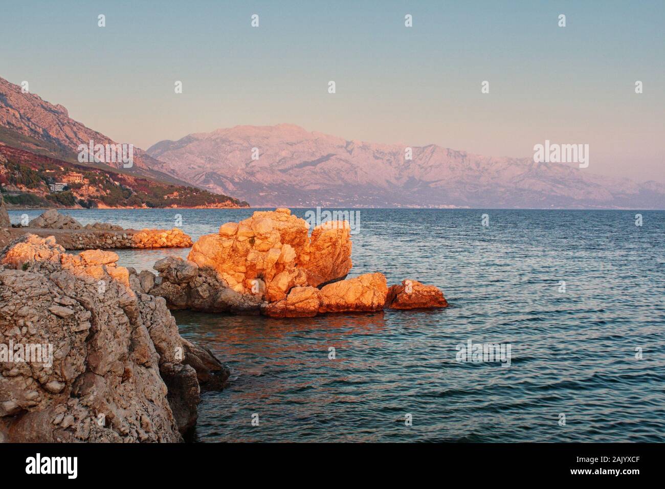 Côte rocheuse de la mer croate, mer et roche en premier plan, falaises et montagnes en arrière-plan, illuminées par le soleil couchant Banque D'Images