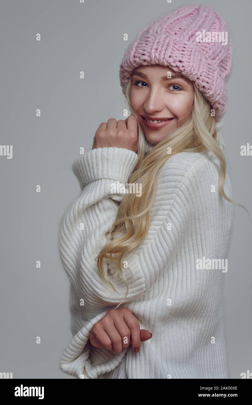 Jeune femme avec de longs cheveux blonds en rose chapeau d'hiver en regardant la caméra avec un fond gris Banque D'Images