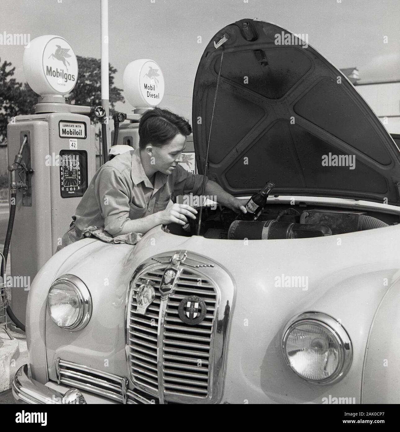 Années 1950, historique, à une station service, un jeune homme attendant un appoint d'huile d'une voiture, England, UK. Banque D'Images