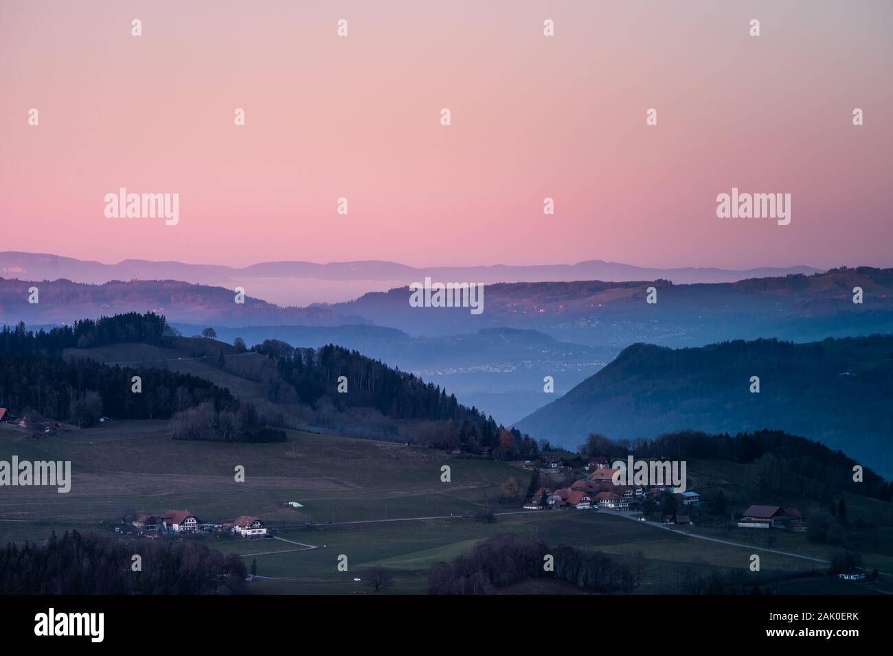 Village entre les collines en Suisse avec ciel rouge et chaude lumière pendant l'heure bleue en hiver Banque D'Images