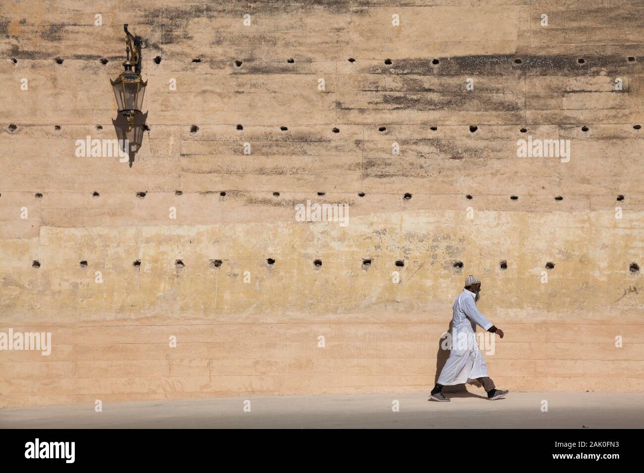 Homme solitaire avec capuchon kufi sur sa tête marchant dans le paysage de l'après-midi des murs de la ville dans la région de Bab Mechouar et Bab Dekkakin à Fes (Fez), Maroc Banque D'Images