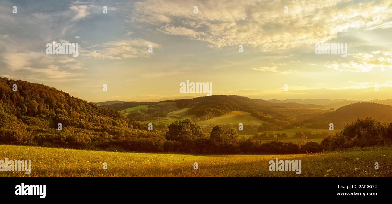 Coucher de soleil sur paysage vallonné, la lueur dorée du soleil couchant, pré au premier plan - panorama pittoresque Banque D'Images