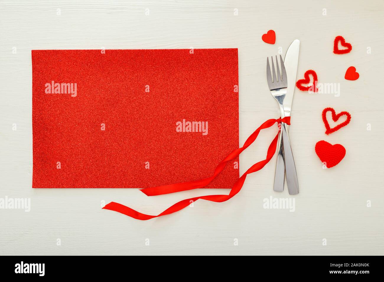 Fatigué de coutellerie par ruban rouge avec beaucoup de coeurs rouges à Jour de Valentines. Table de fête, sur une table en bois blanc. Dîner au restaurant Banque D'Images