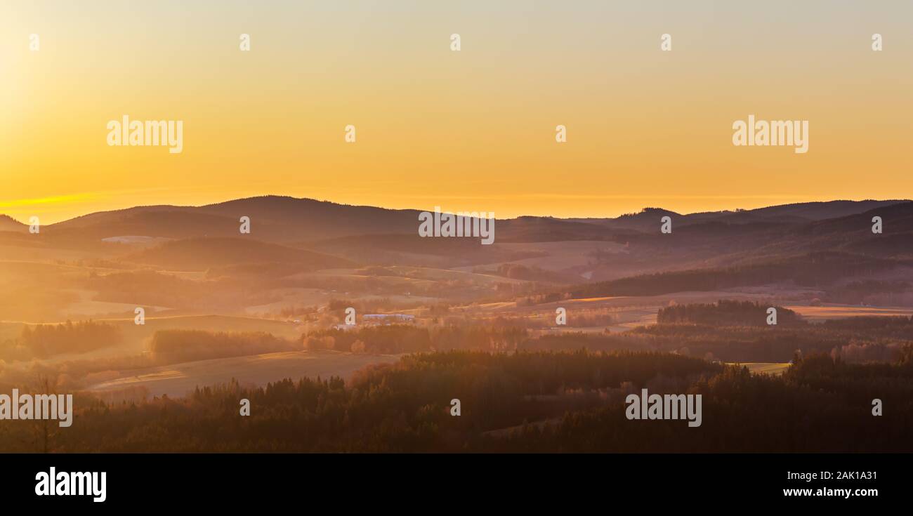 lever du soleil dans les montagnes - paysage vallonné avec prairies et forêts dans un dédale, dans un ciel jaune et orange Banque D'Images