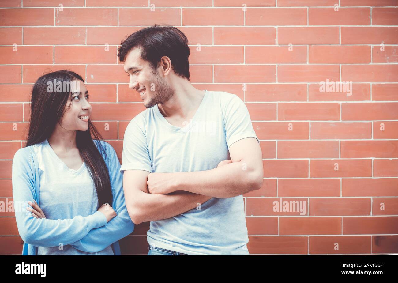Jeune couple attrayant d'Asie à la face et sourit tout en se tenant dos à dos contre le mur de briques avec romantique. Banque D'Images