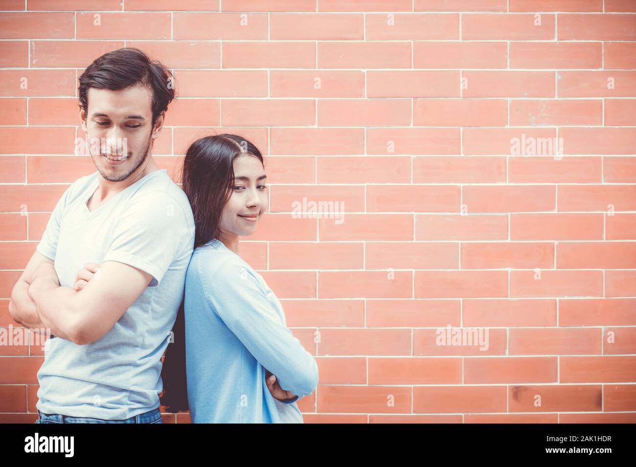 Jeune couple attrayant d'Asie à la face et sourit tout en se tenant dos à dos contre le mur de briques avec romantique. Banque D'Images