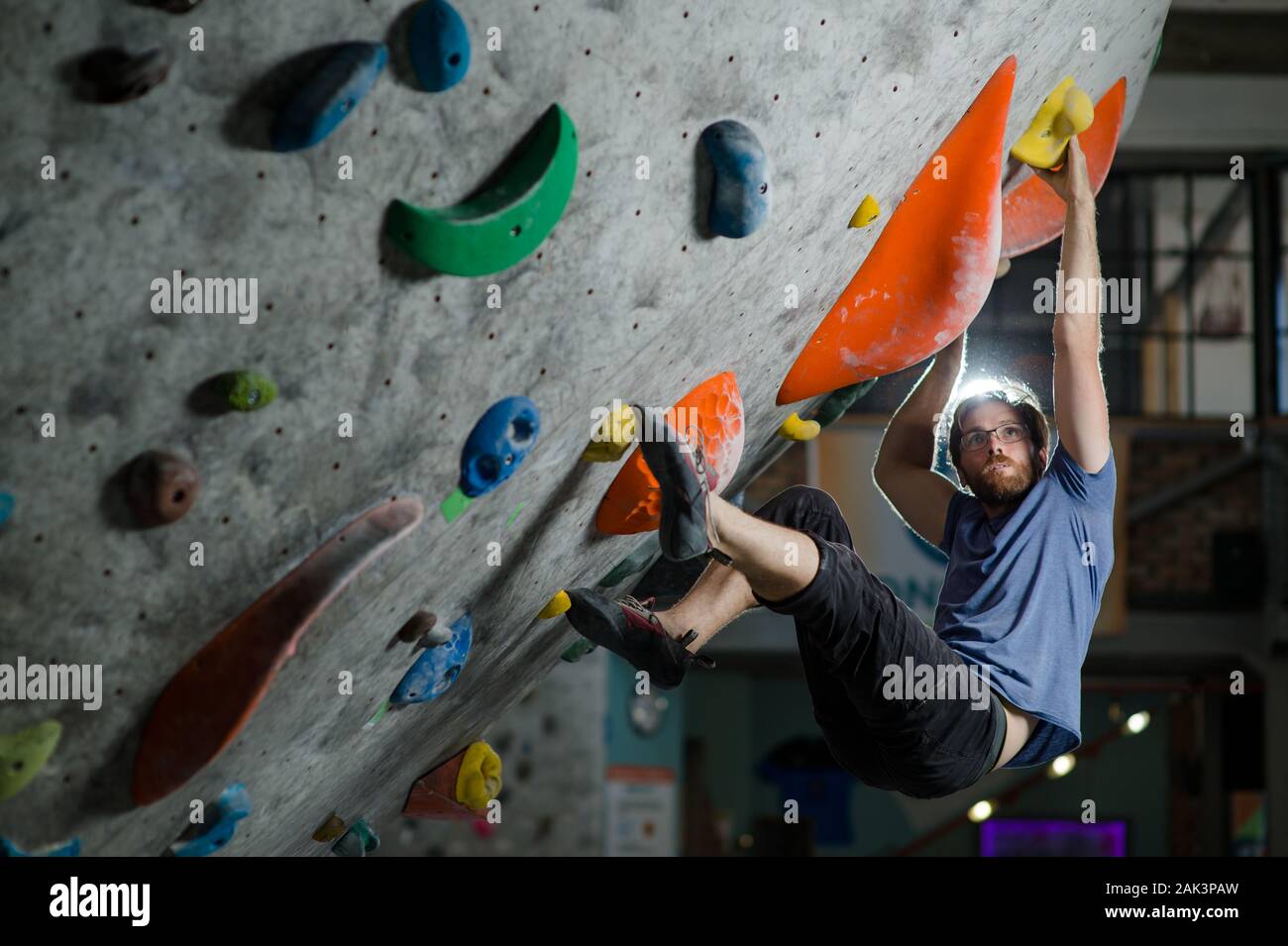 Jeune active sport portrait homme barbu à lunettes et t-shirt d'Escalade sur mur avec color détient au cours de session de formation de bloc Banque D'Images