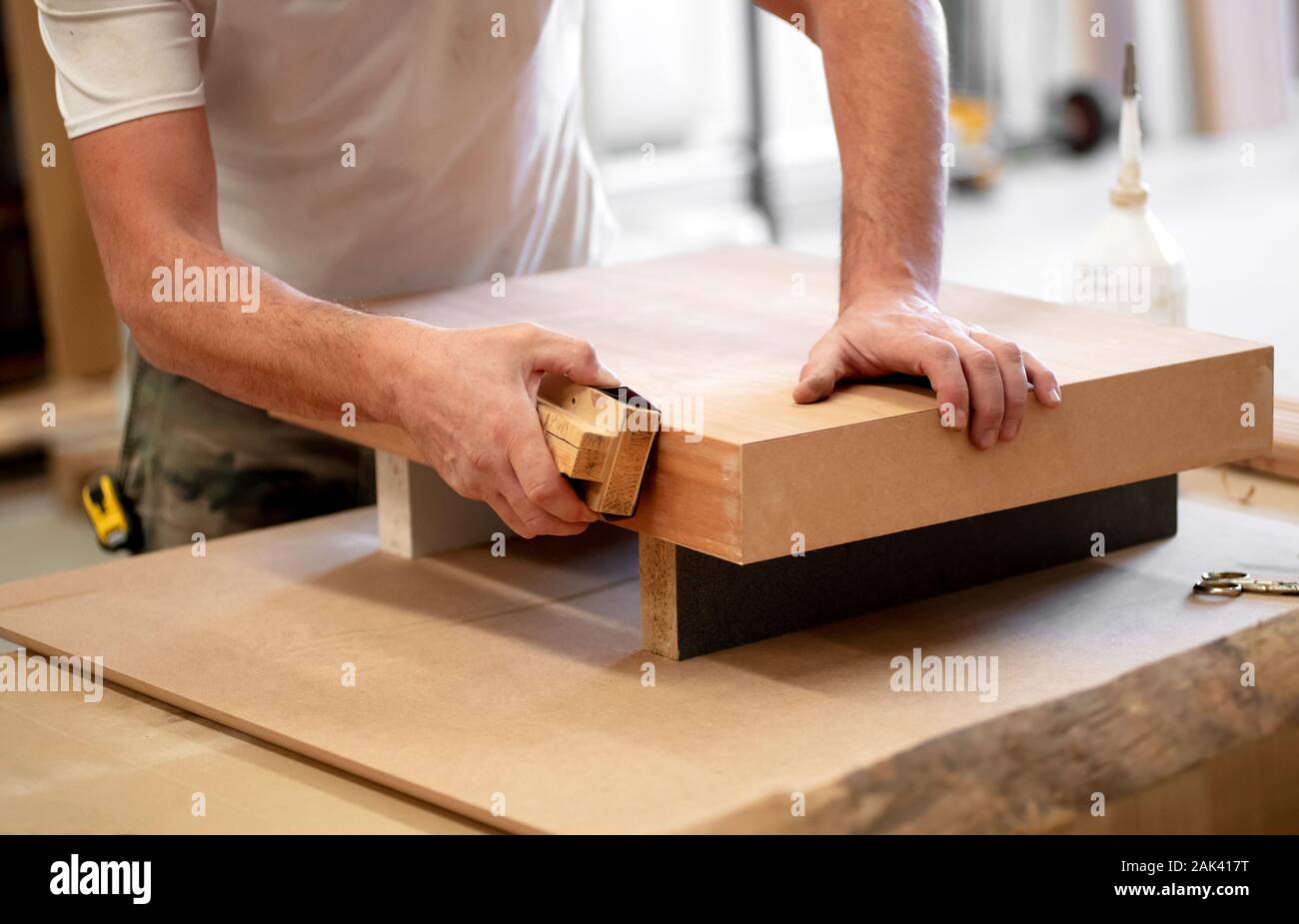 Mains d'un menuisier de ponçage manuellement le bord d'un bloc de bois avec du papier de verre sur un outil à main dans un atelier de menuiserie bois ou Banque D'Images
