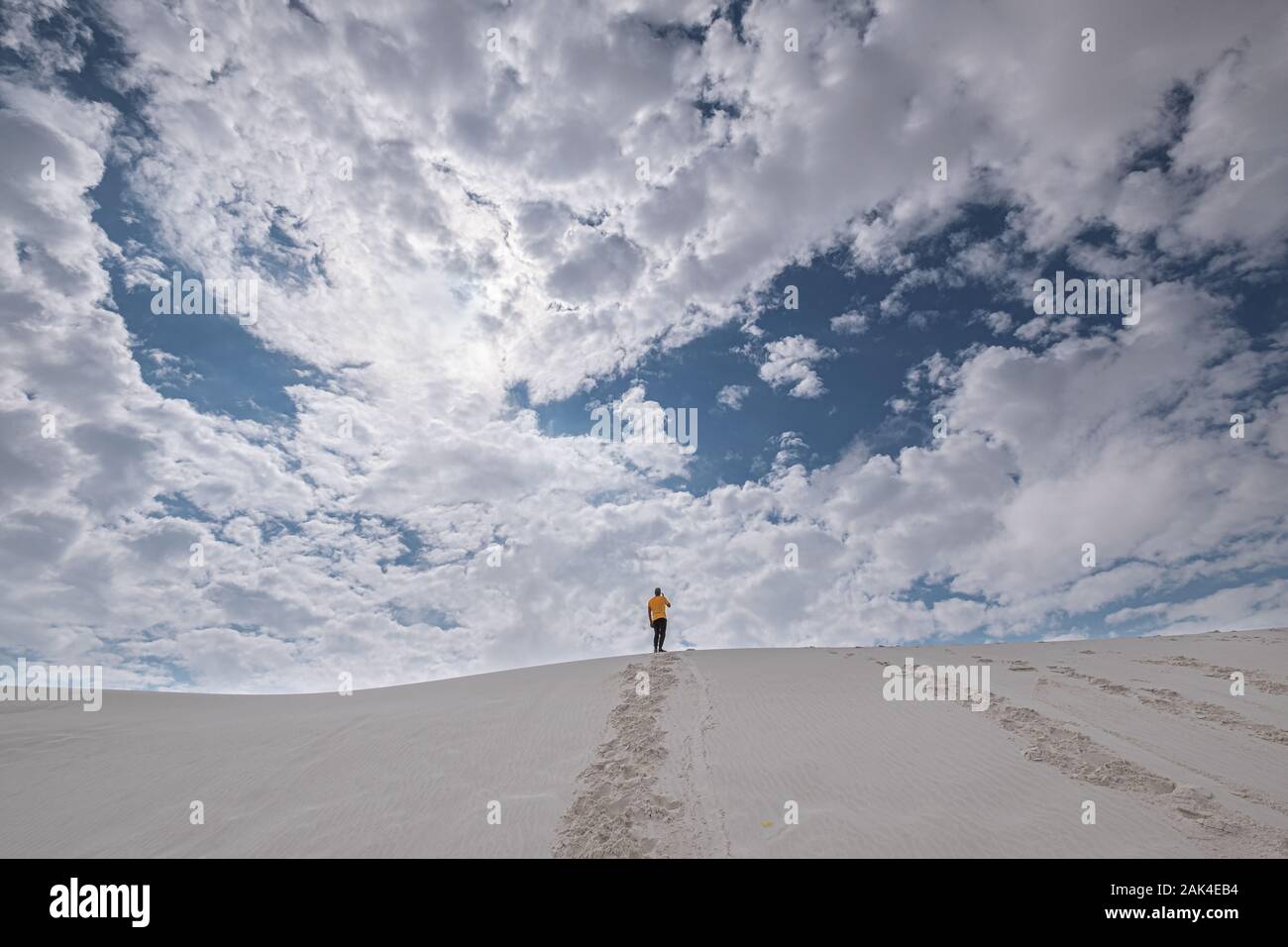 Vue arrière d'un homme en jaune t-shirt debout sur une dune de sable dans la distance contre ciel dramatique Banque D'Images