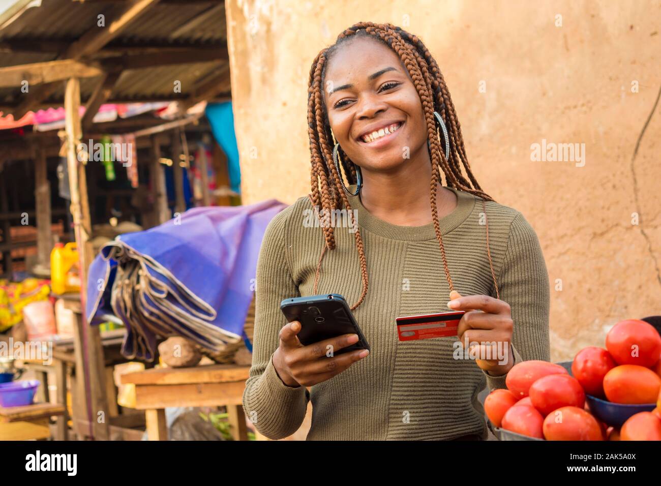 Dame nigériane vendre dans un marché local en utilisant son téléphone portable et carte de crédit pour faire une transaction en ligne smiling Banque D'Images